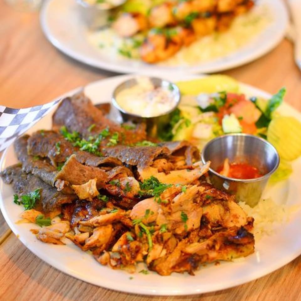 A plate of Gyros and Tzatziki's kebab with rice, salad, and two dipping sauces.
