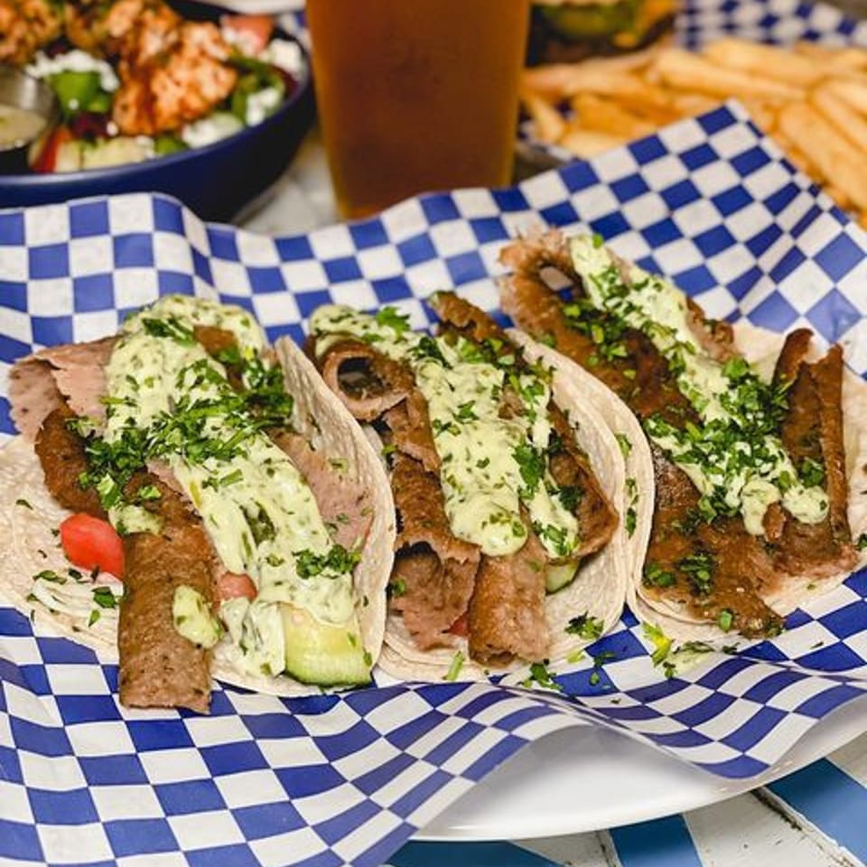 Three Gyros and Tzatziki kebab tacos with sauce and cilantro on blue and white checkered paper.