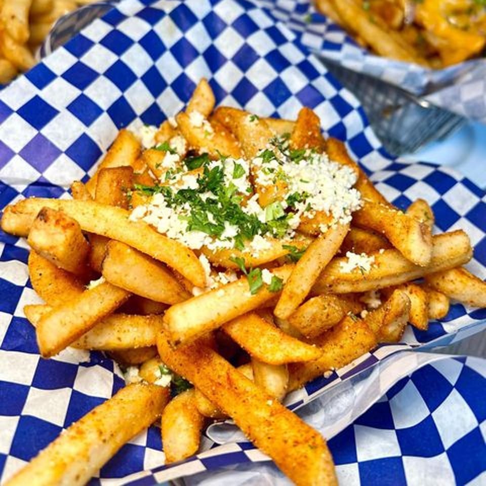 Seasoned fries topped with crumbled feta cheese and fresh parsley in a blue and white checkered basket.