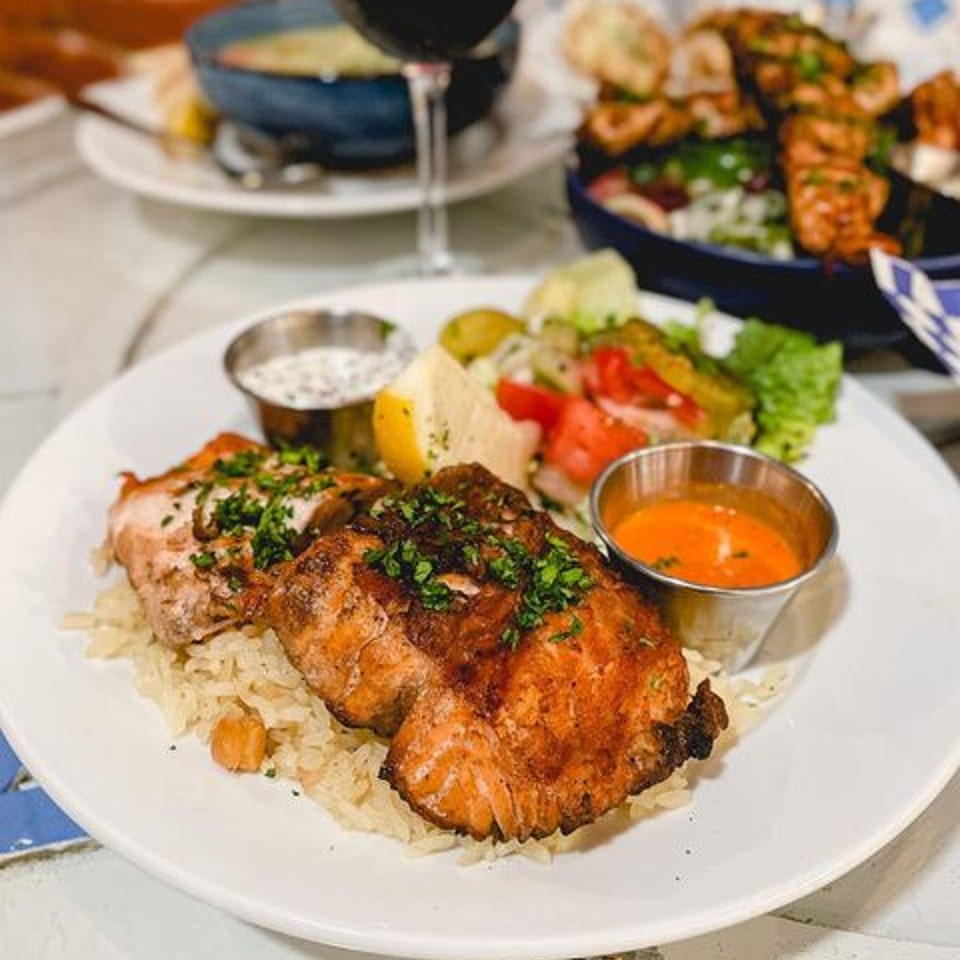 Grilled salmon kebab with rice, salad, lemon, and dipping sauces on a white plate.